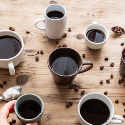 Várias chávenas e canecas de café com café preto sobre mesa de madeira com grãos de café