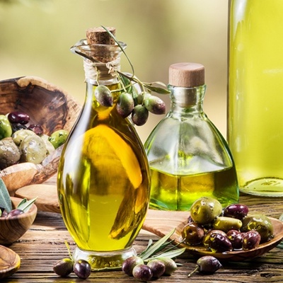 Garrafas de azeite e azeitonas em mesa de madeira com ramos de oliveira