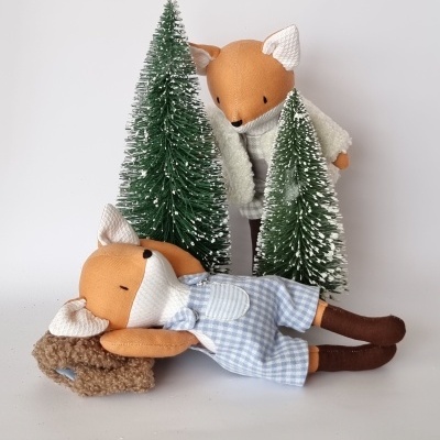 Duas bonecas de raposa de tecido com duas árvores artificiais de Natal ao fundo