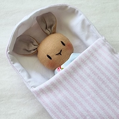 Boneco de coelho de tecido num saco de dormir riscado rosa e branco