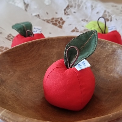 Maçãs decorativas em tecido vermelho com folhas verdes numa tigela de madeira