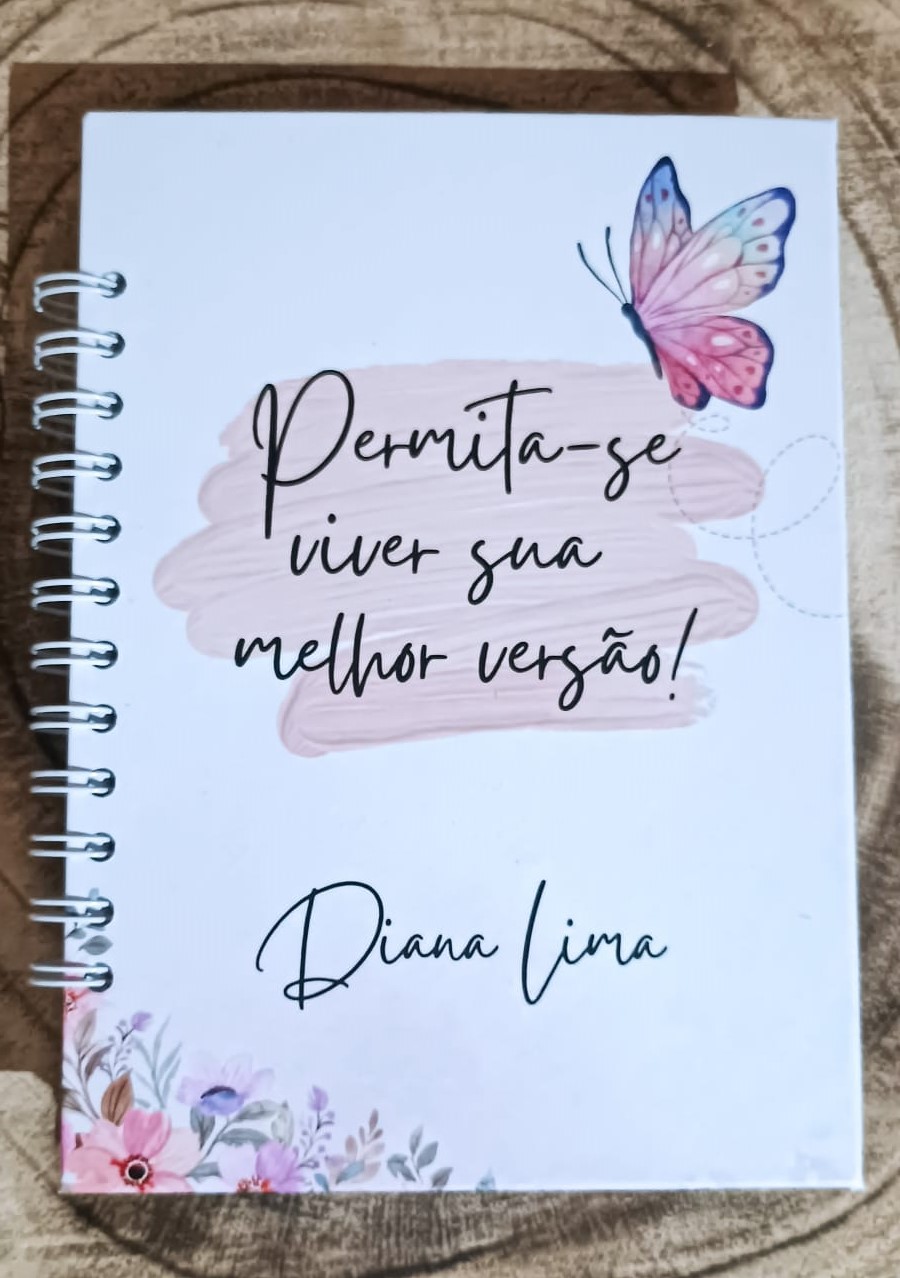 Caderno branco com borboleta rosa e azul e texto motivacional em português