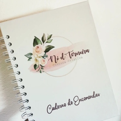 Caderno branco com capa decorada, texto e flores, encadernação espiral e mão segurando.