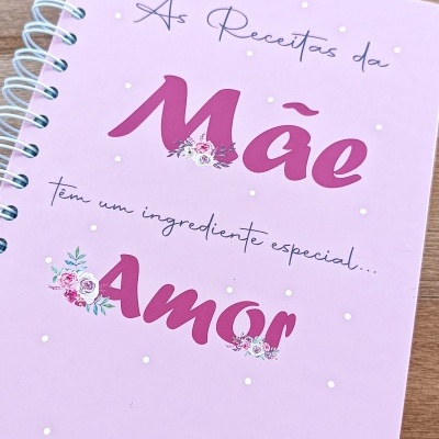Caderno rosa claro com texto e decoração floral sobre mesa de madeira clara