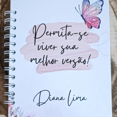 Caderno branco com borboleta rosa e azul e texto motivacional em português