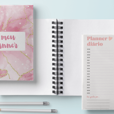 Planner rosa com padrão dourado e página diária aberta com lápis e prato ao lado