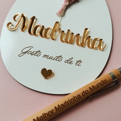 Placa decorativa branca com texto dourado para madrinha, flores secas e caneta de madeira gravada.