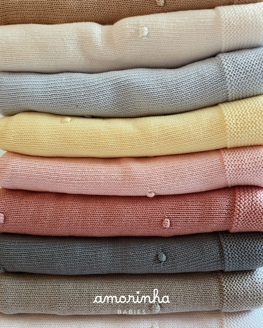 Roupa de bebé em malha em várias cores suaves empilhadas