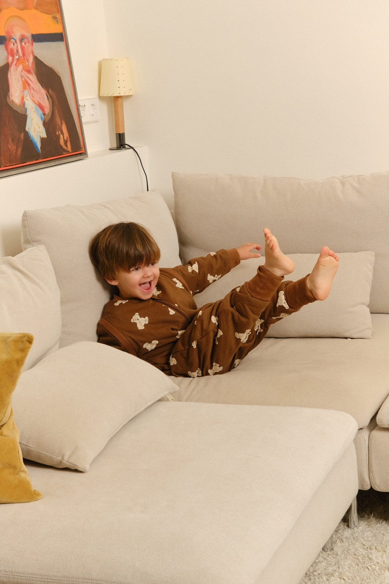 Criança sorridente no sofá creme com pijama castanho de ursos