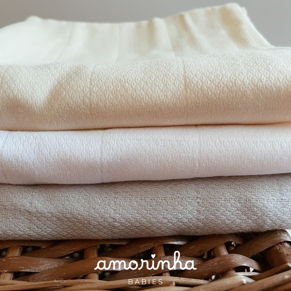 Três panos dobrados em tons neutros sobre vime, com texto amorinha BABIES