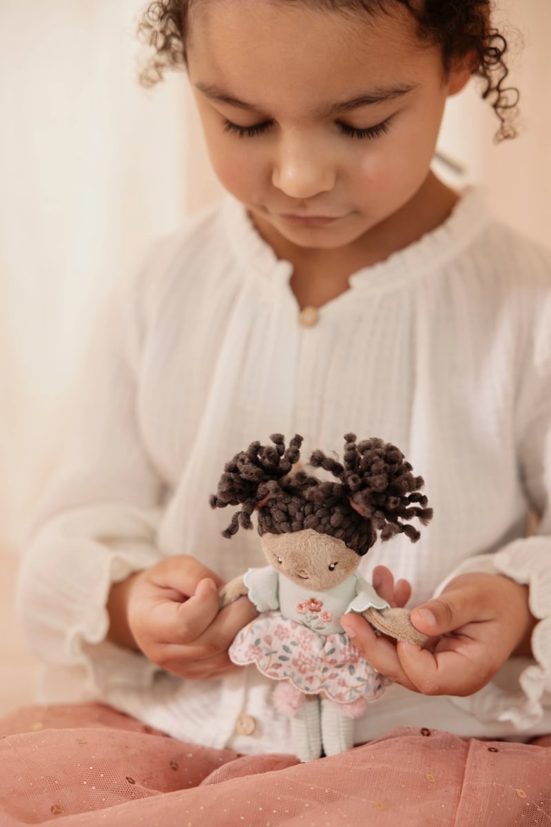 Menina com blusa branca segurando boneca de trapos com vestido azul e rosa.