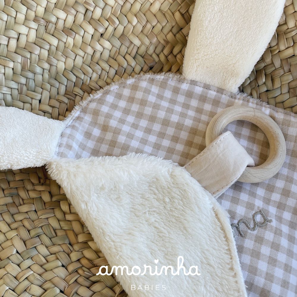 Produto de bebé com tecido aos quadrados, tecido peludo branco e anel de madeira