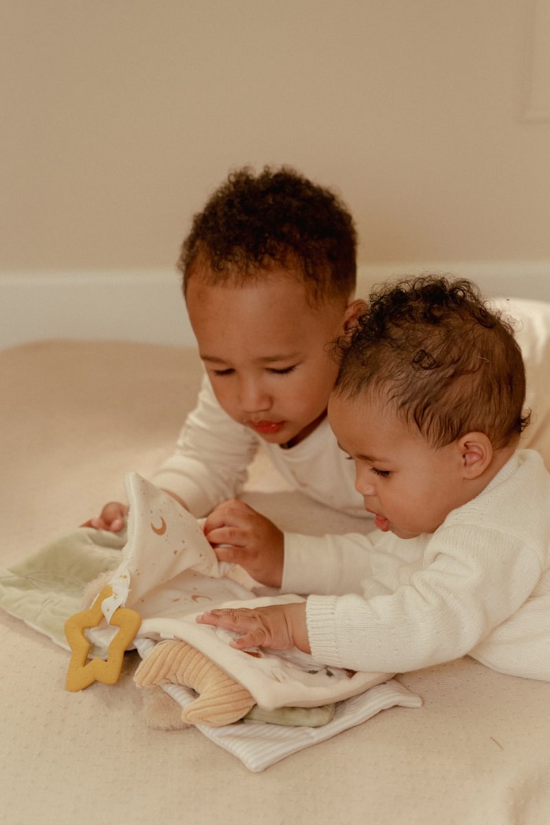 Bebés a interagir com um livro de tecido e mordedor em superfície bege