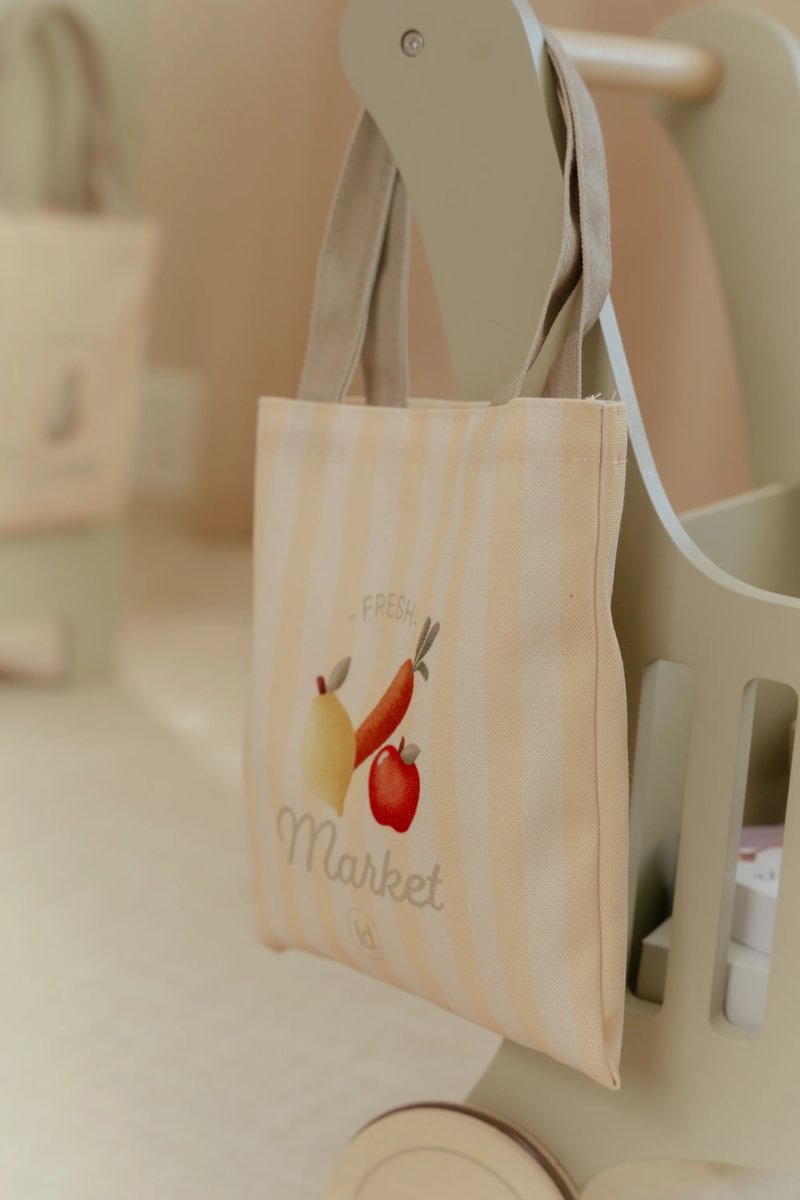 Saco de tecido com desenho de frutas e texto pendurado num carrinho de madeira