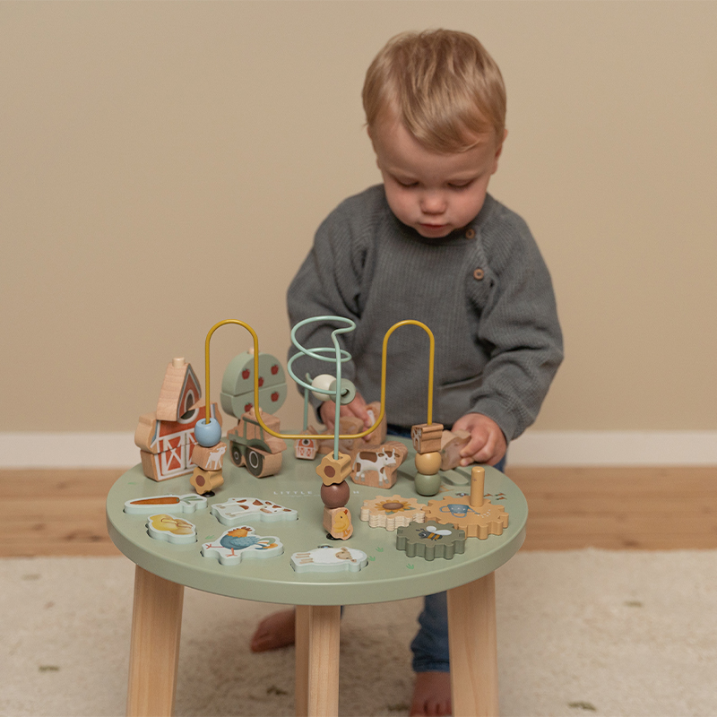 Criança pequena a brincar com mesa de madeira e brinquedos coloridos em ambiente interior