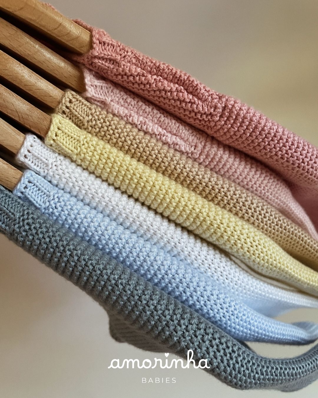 Roupas de malha coloridas para bebés penduradas em cabides de madeira