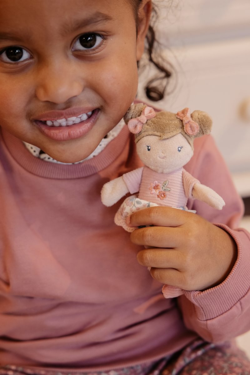Menina a sorrir segurando uma boneca de pano com vestido rosa e cabelo em coques.