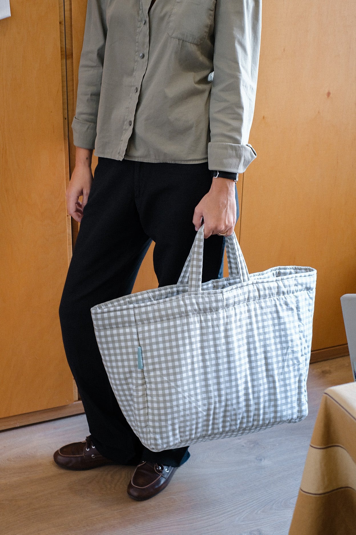 Bolsa têxtil xadrez cinza e branco grande, homem a segurar, interior com porta de madeira
