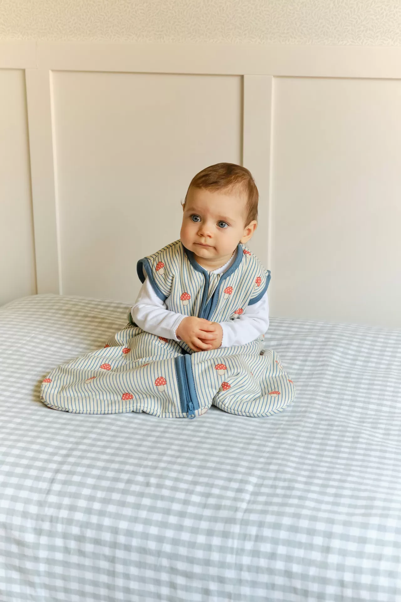 Bebé sentado numa cama com saco de dormir listrado azul claro e branco com padrões vermelhos