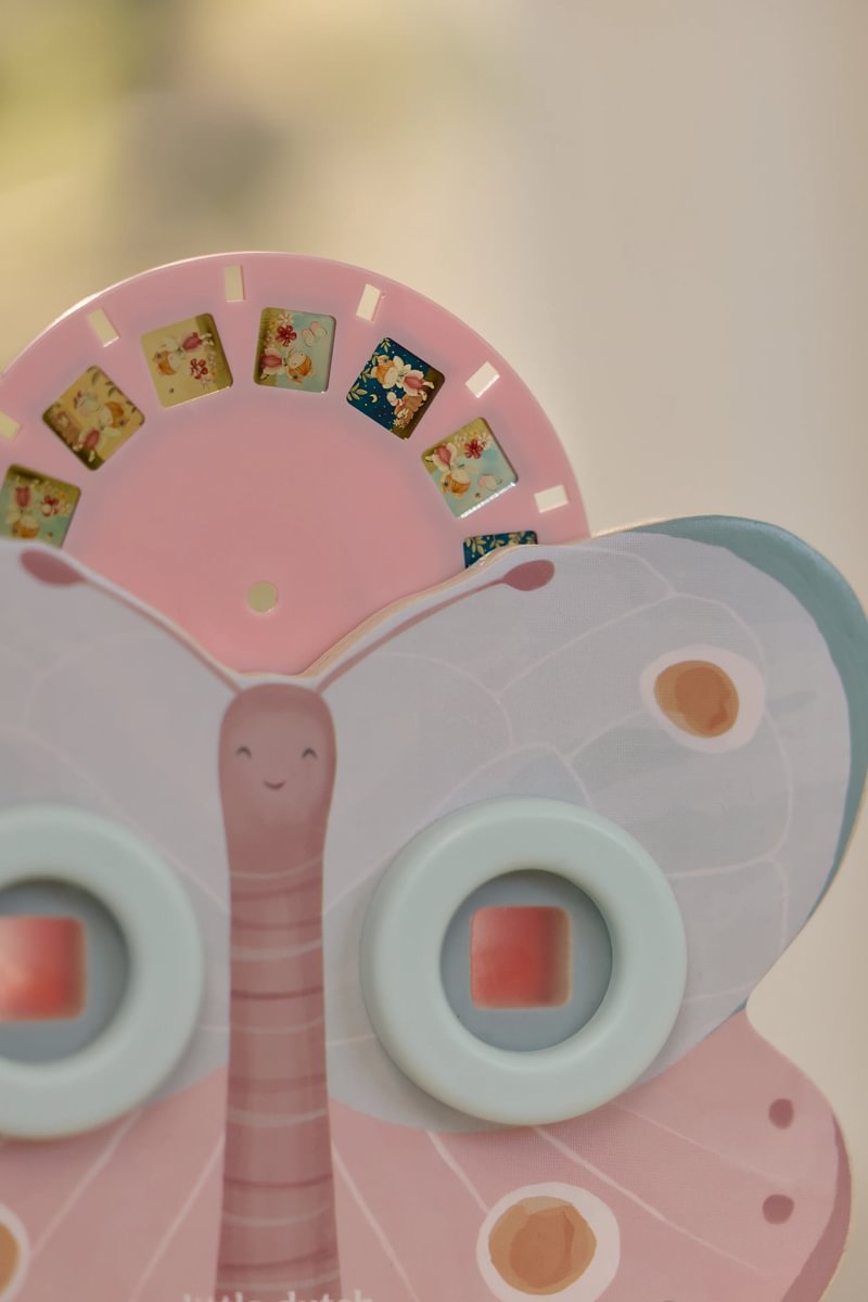 Brinquedo borboleta infantil com lentes azuis e disco rosa com imagens coloridas.