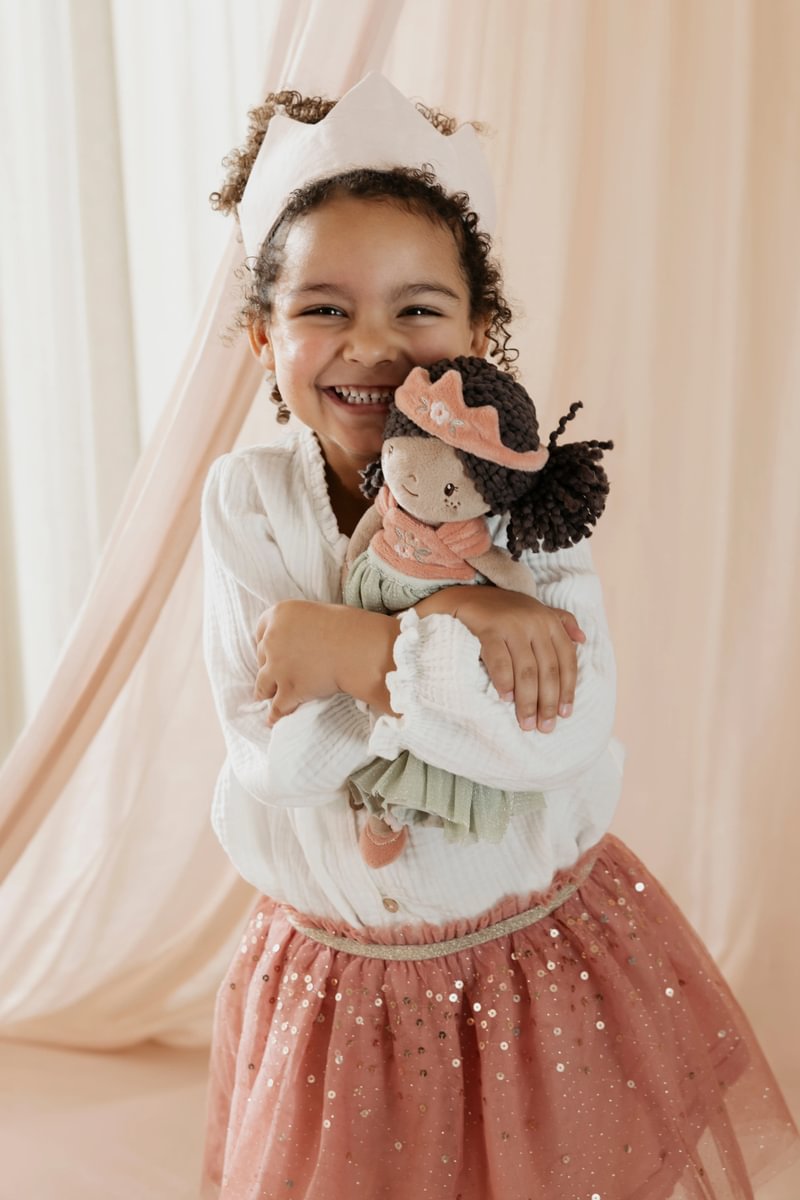 Menina sorridente com vestido de tule rosa e blusa branca segurando boneca de tecido com roupa verde e rosa.