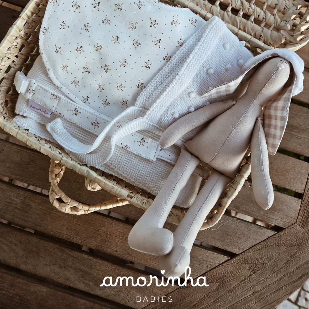 Cesto com mantas brancas e boneco tecido em superficie de madeira.