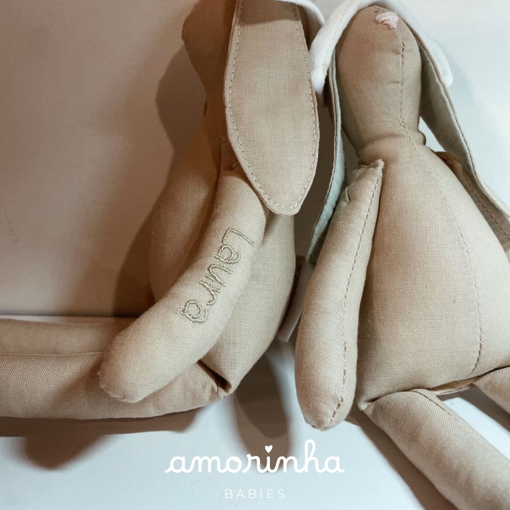 Peluches de coelho bege em tecido com nome bordado e logo amorinha BABIES no fundo branco
