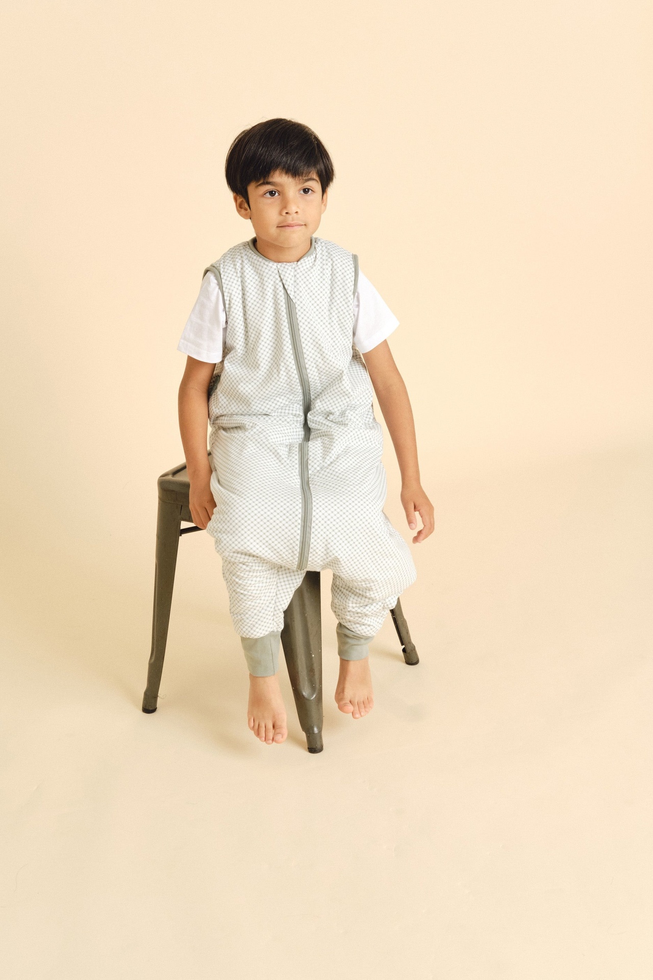 Criança sentada numa cadeira usando saco de dormir quadriculado cinza e branco