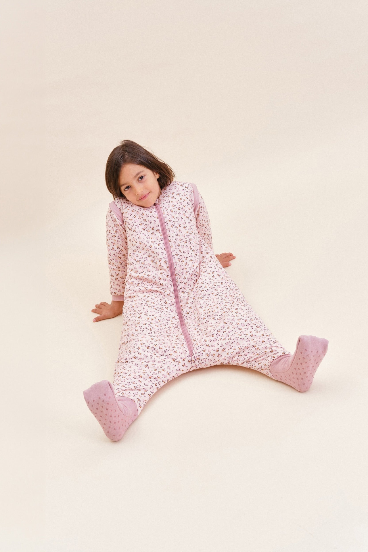 Menina a usar saco de dormir com padrão floral rosa claro.