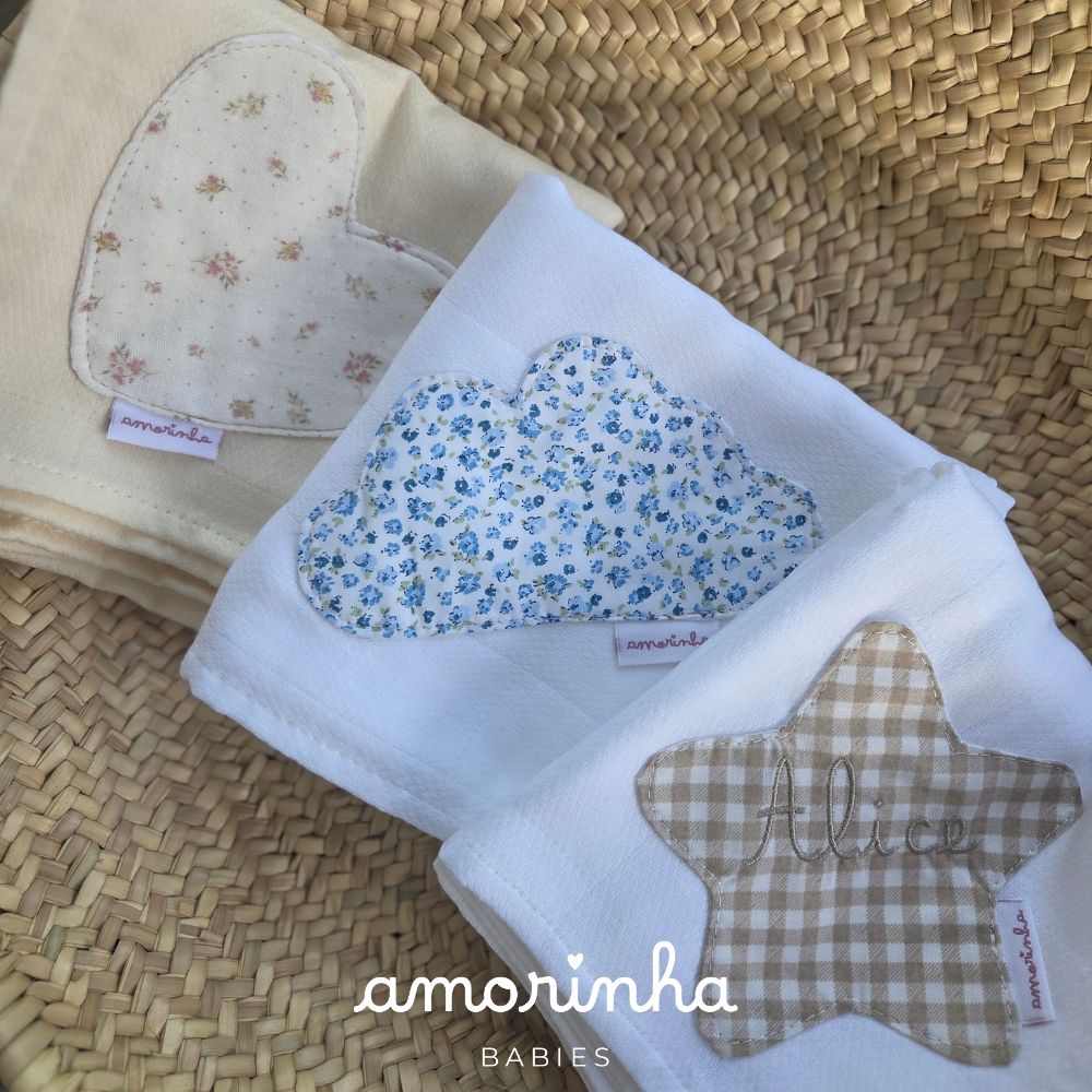 Três mantas de bebé com diferentes aplicações e etiquetas amorinha sobre cesta de vime.