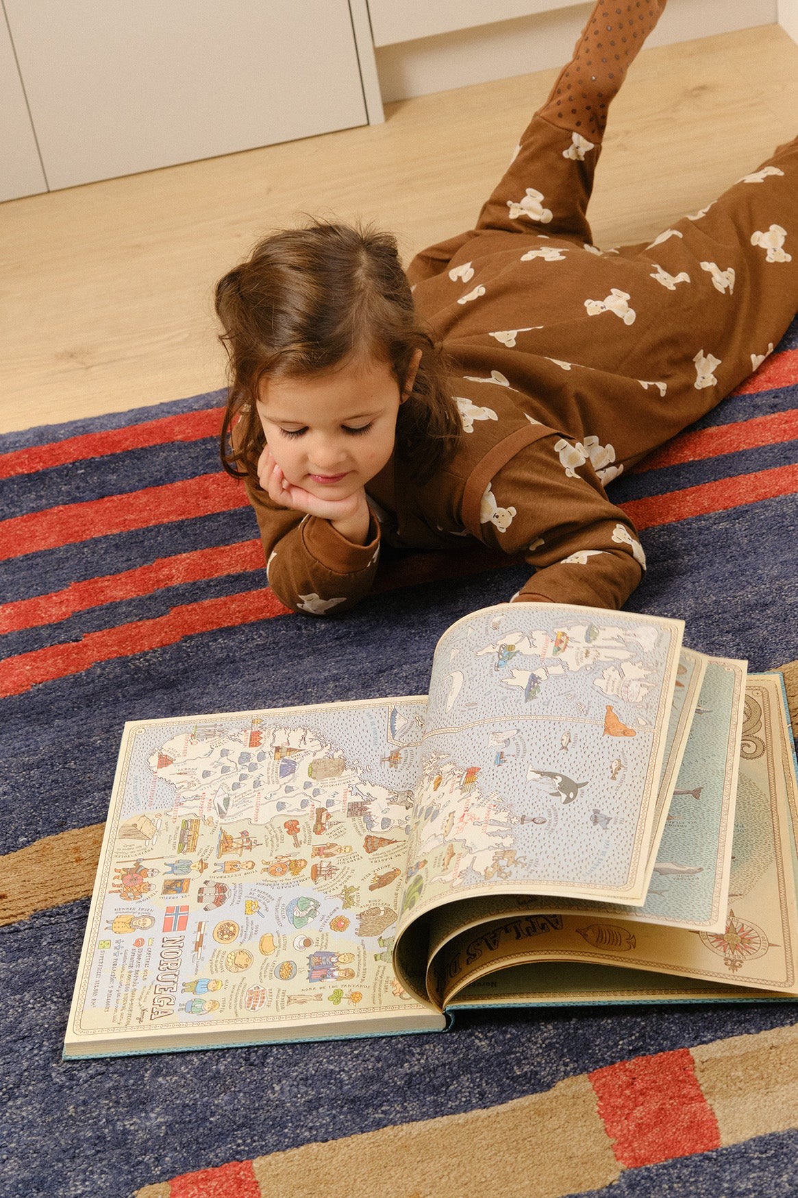 Menina deitada a ler livro com mapa ilustrado no tapete
