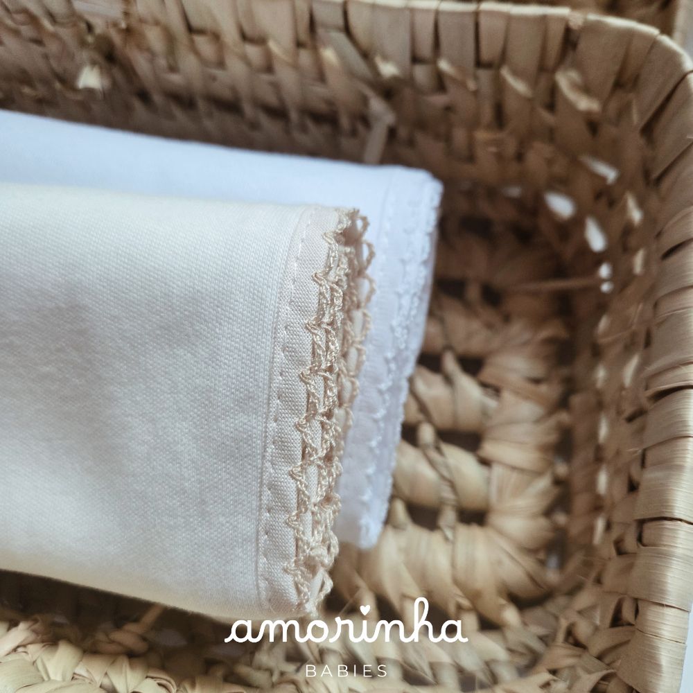 Toalhas de tecido branco e bege com bordado delicado dentro de cesto de vime