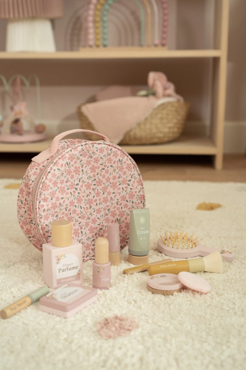 Estojos e produtos de cosmética infantil em tons rosa, creme e verde claros sobre tapete creme, com estojo florido