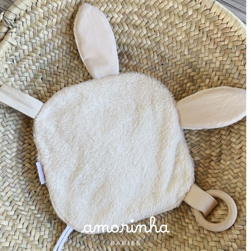 Produto de bebé branco felpudo com orelhas e anel de madeira dentro de cesta de palha