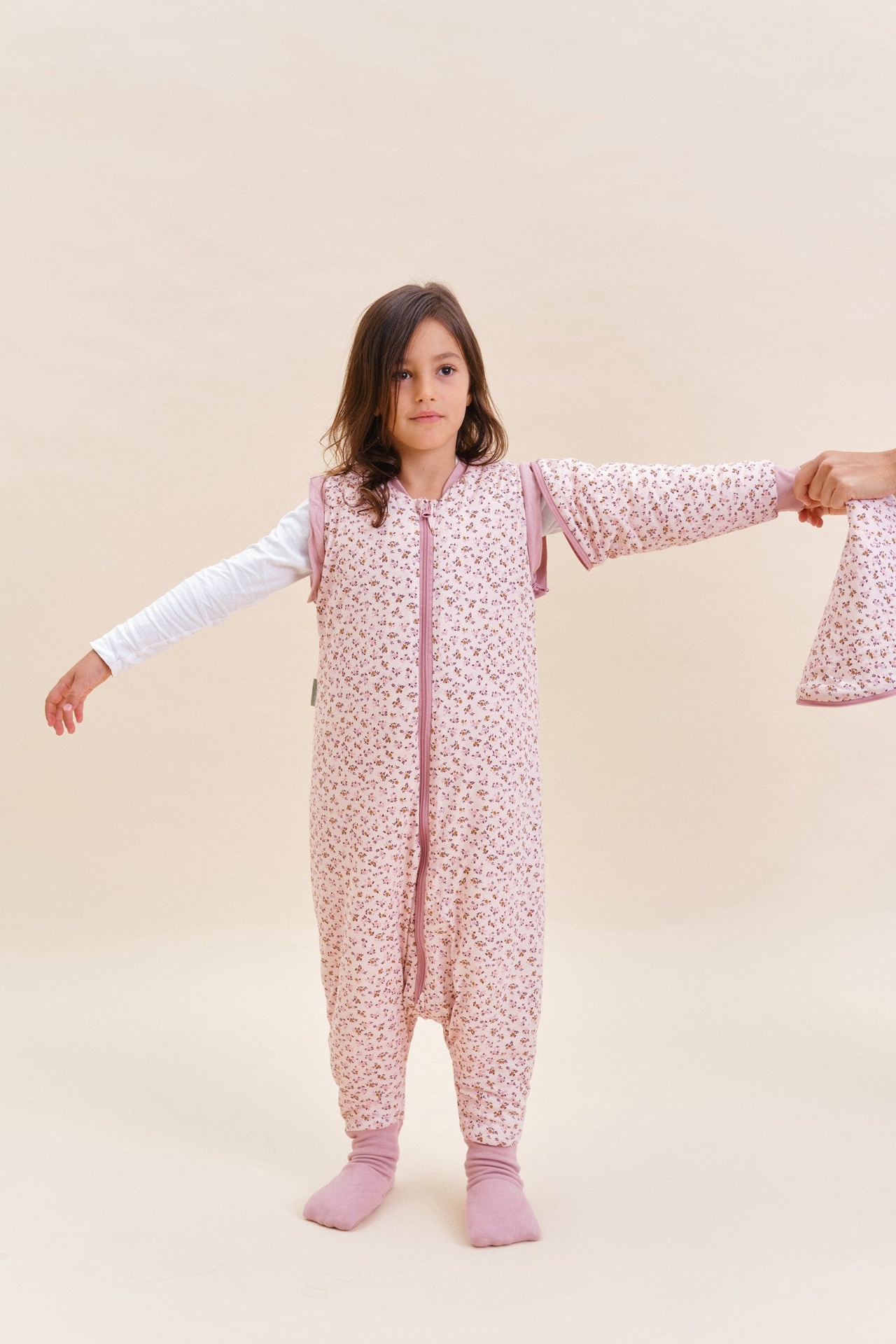 Criança com saco de dormir rosa com padrão floral e manga destacável