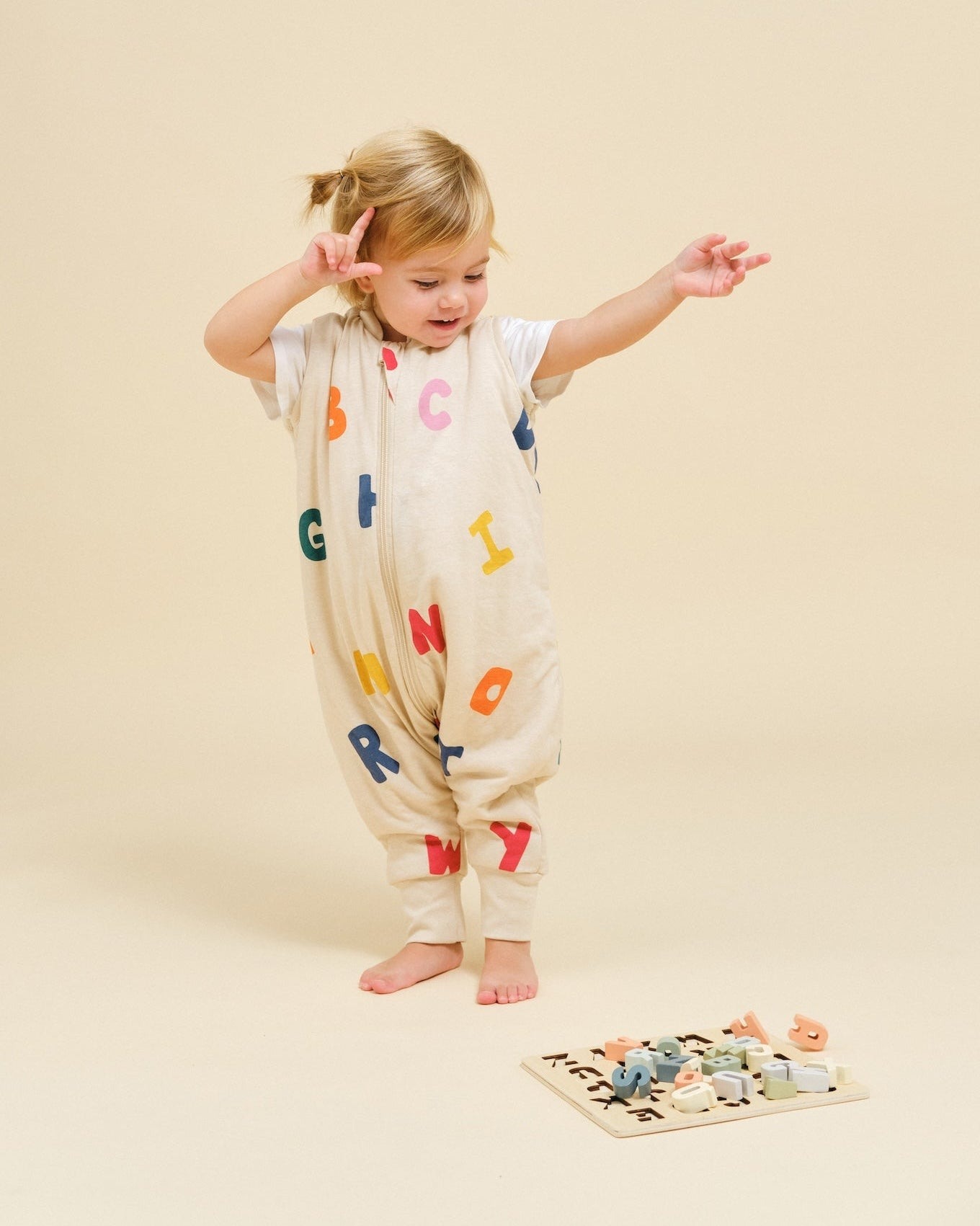 Criança com babygrow com letras coloridas e tabuleiro de letras no chão