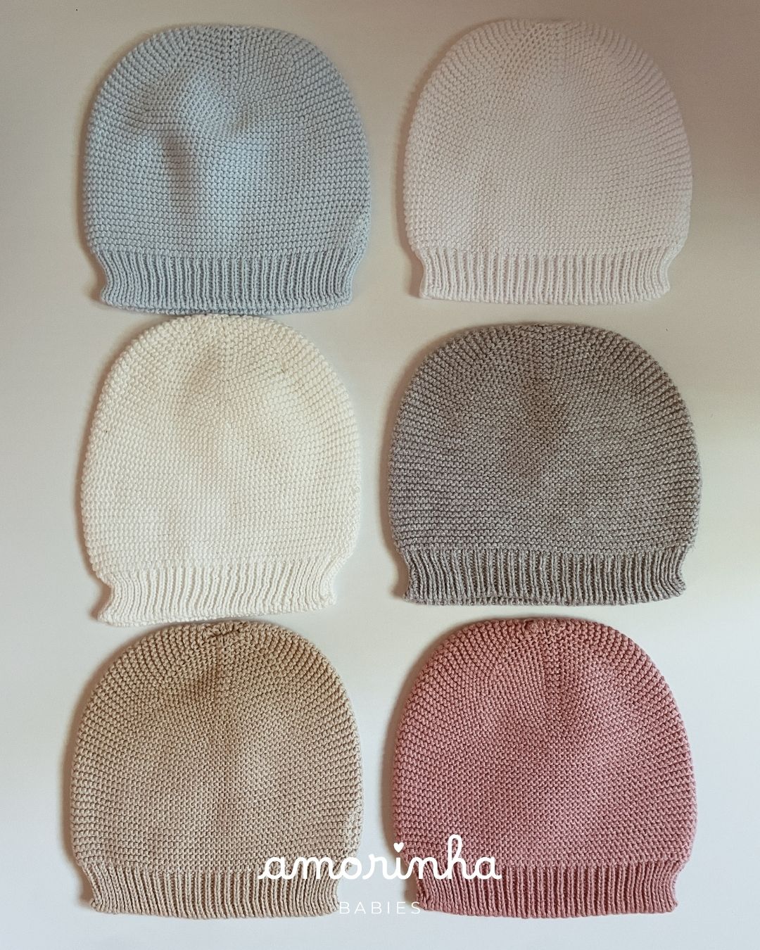 Seis gorros de malha coloridos para bebés sobre fundo claro com texto amorinha BABIES