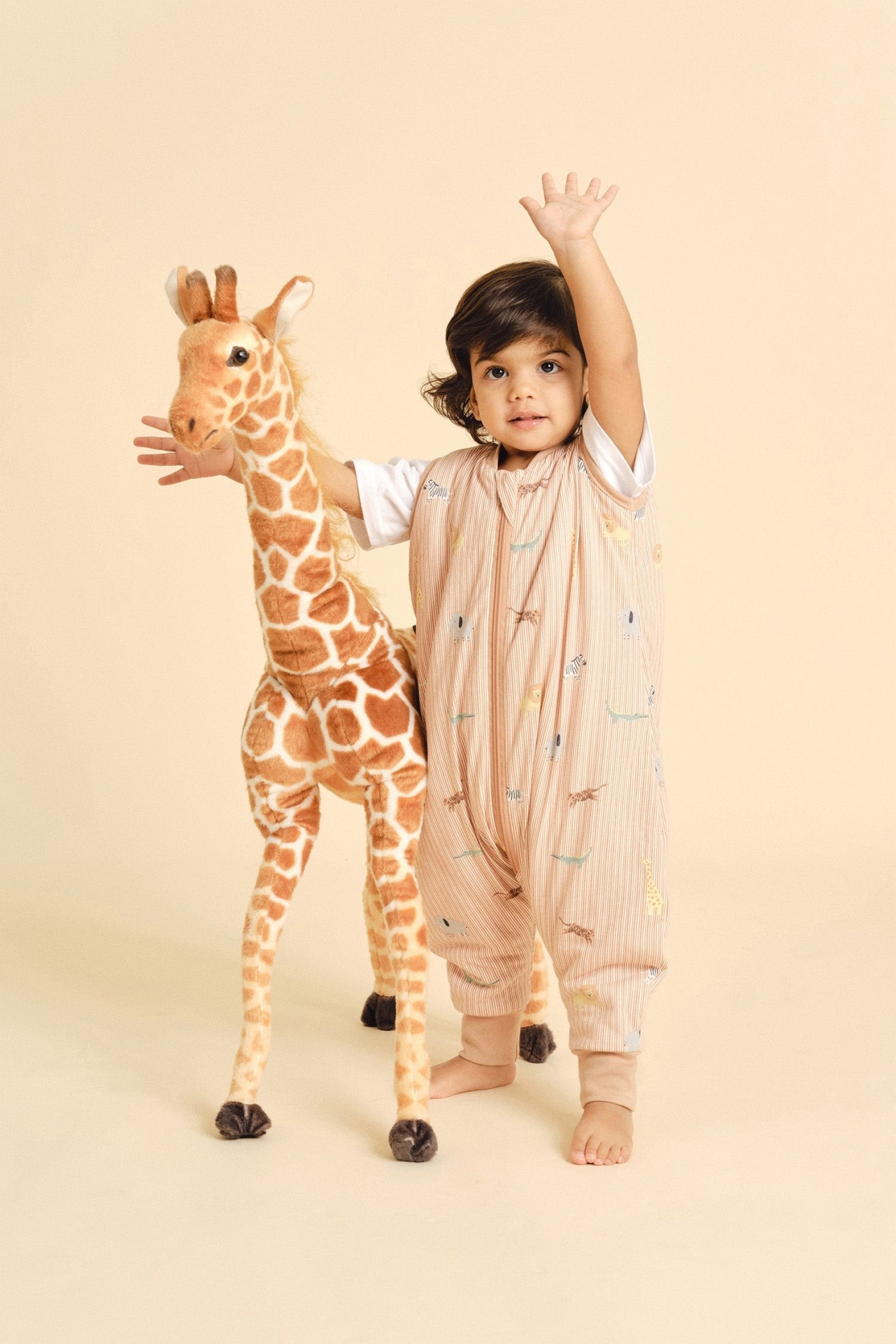 Criança com pijama colorido ao lado de peluche de girafa num fundo bege