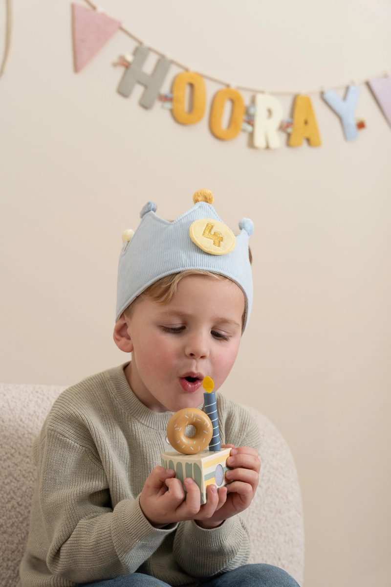 Criança com coroa azul e bolo de madeira com vela azul