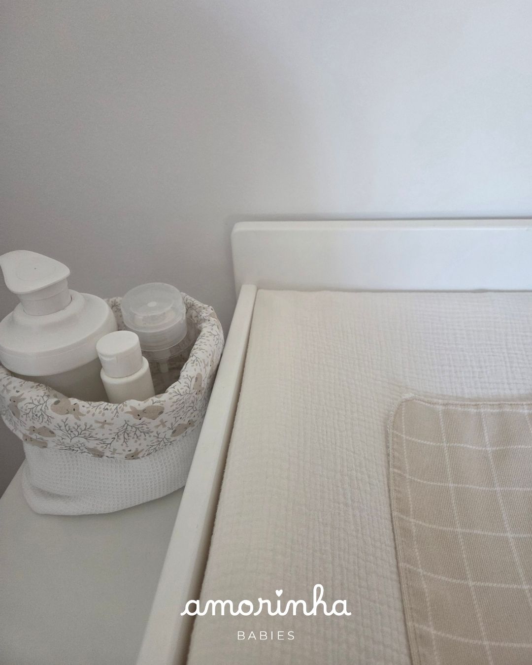 Cesto de tecido com frascos e berço branco com almofada creme