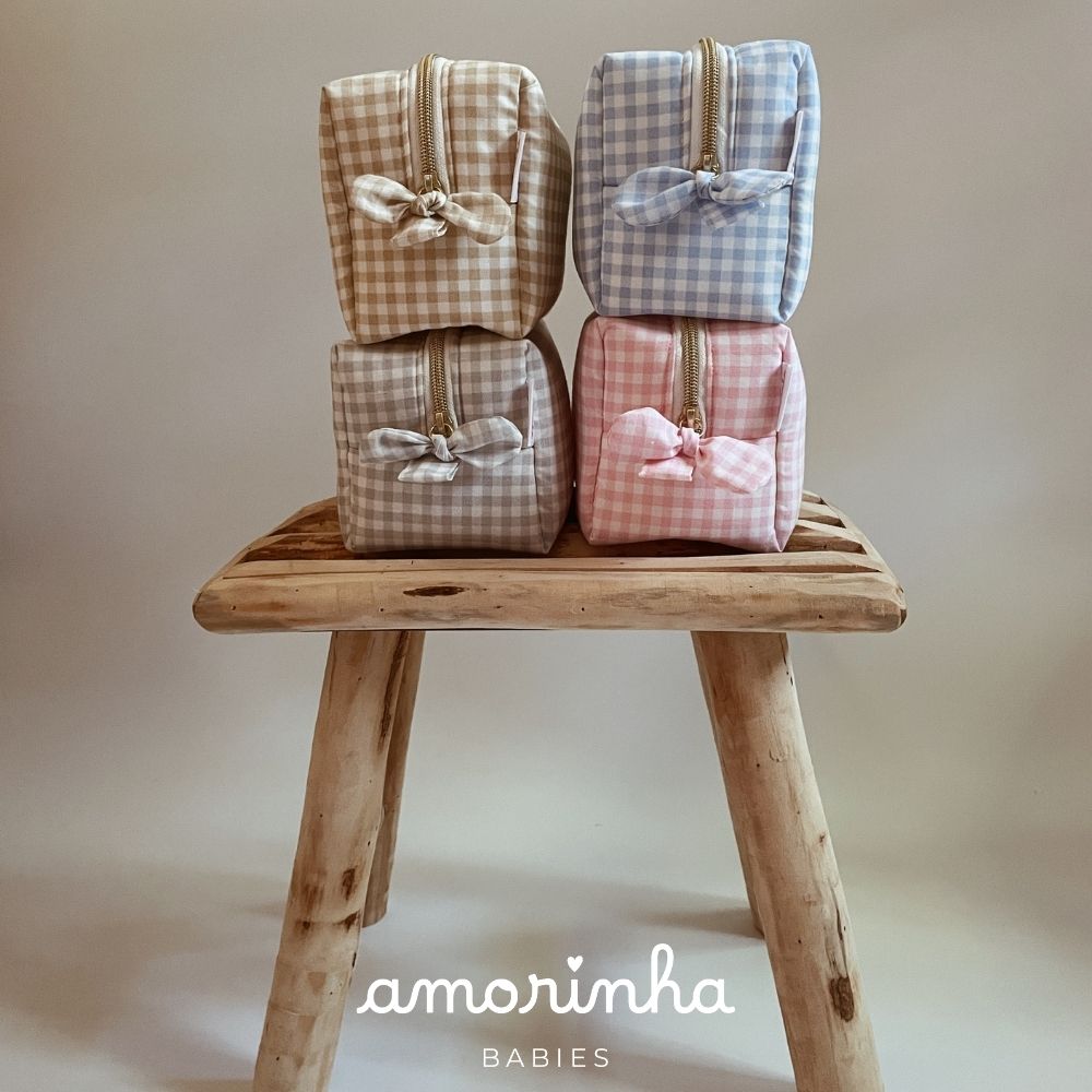 Quatro bolsas de tecido xadrez nas cores bege, azul, cinza e rosa sobre banco de madeira