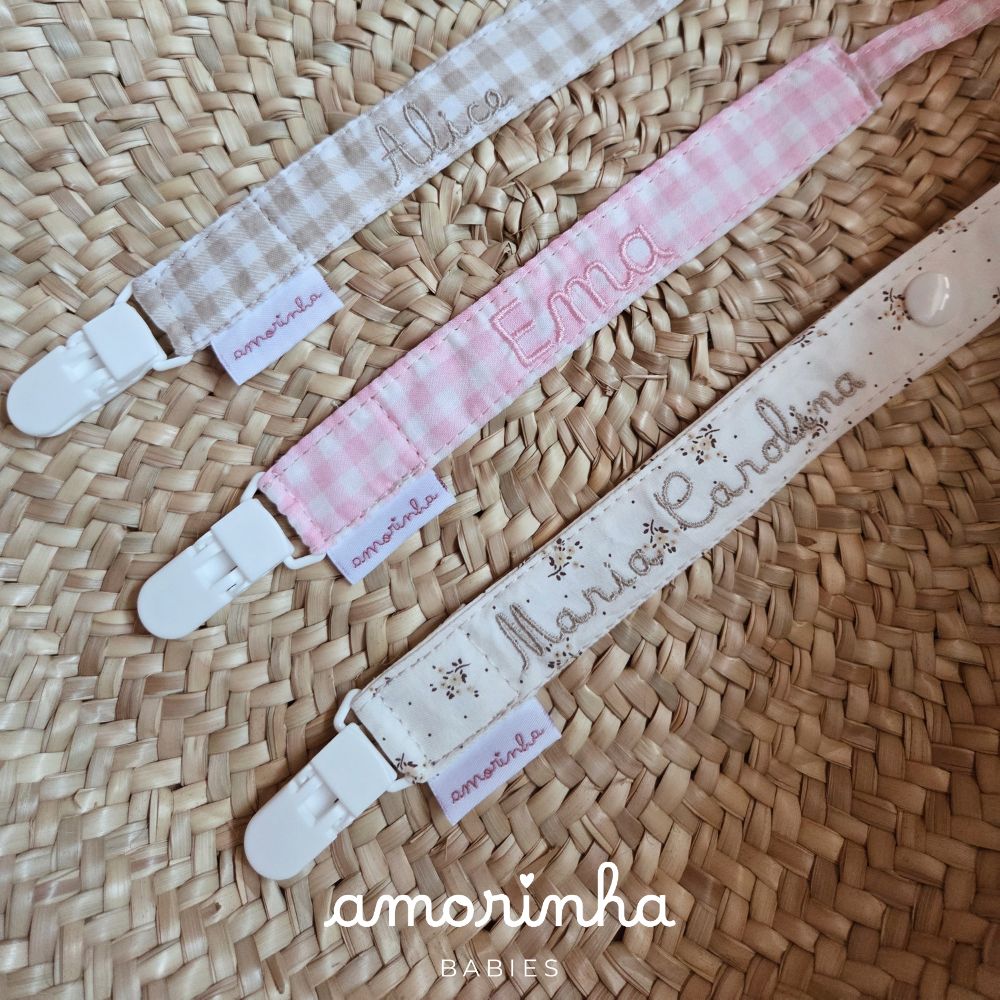 Fitas para chupeta personalizadas com nomes bordados em tecidos coloridos sobre tapete de palha