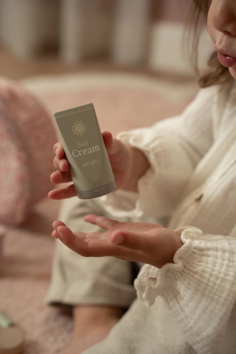 Criança segurando tubo de creme solar Sun Cream SPF 30+ 100 ml com camisola branca de malha