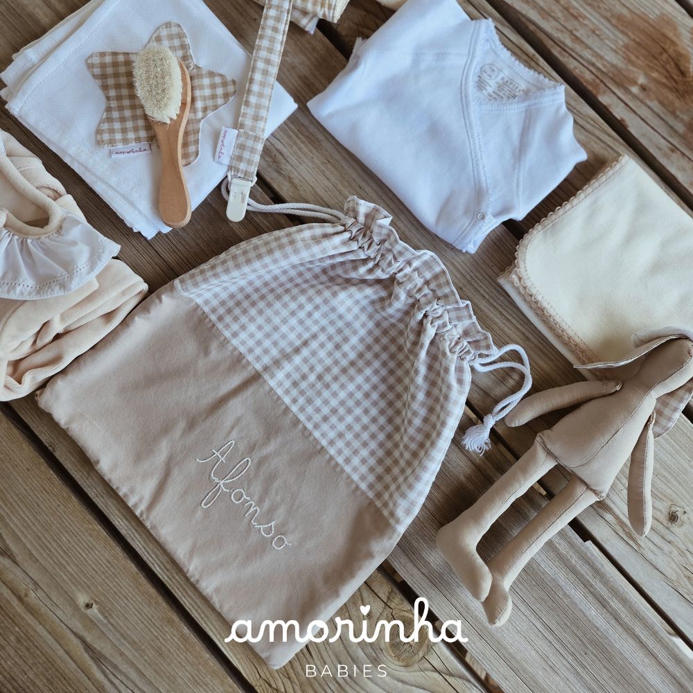 Conjunto de acessórios para bebé com saco personalizado, babete, chupeta, body, manta e boneco sobre madeira