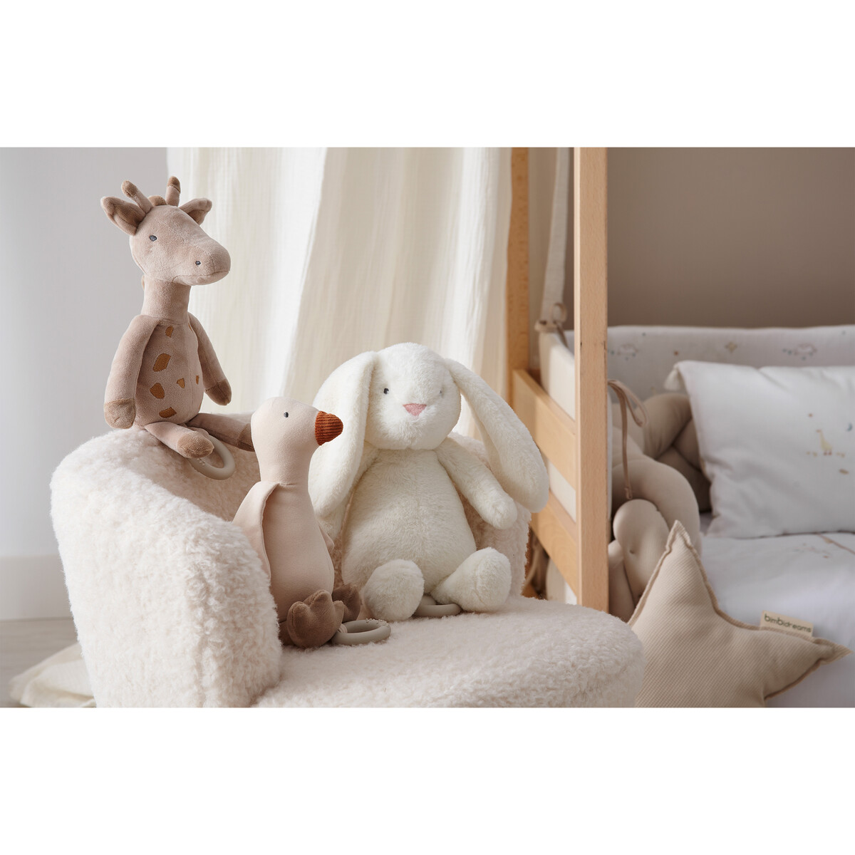 Três peluches sentados numa poltrona creme junto a um berço com almofada estrela.