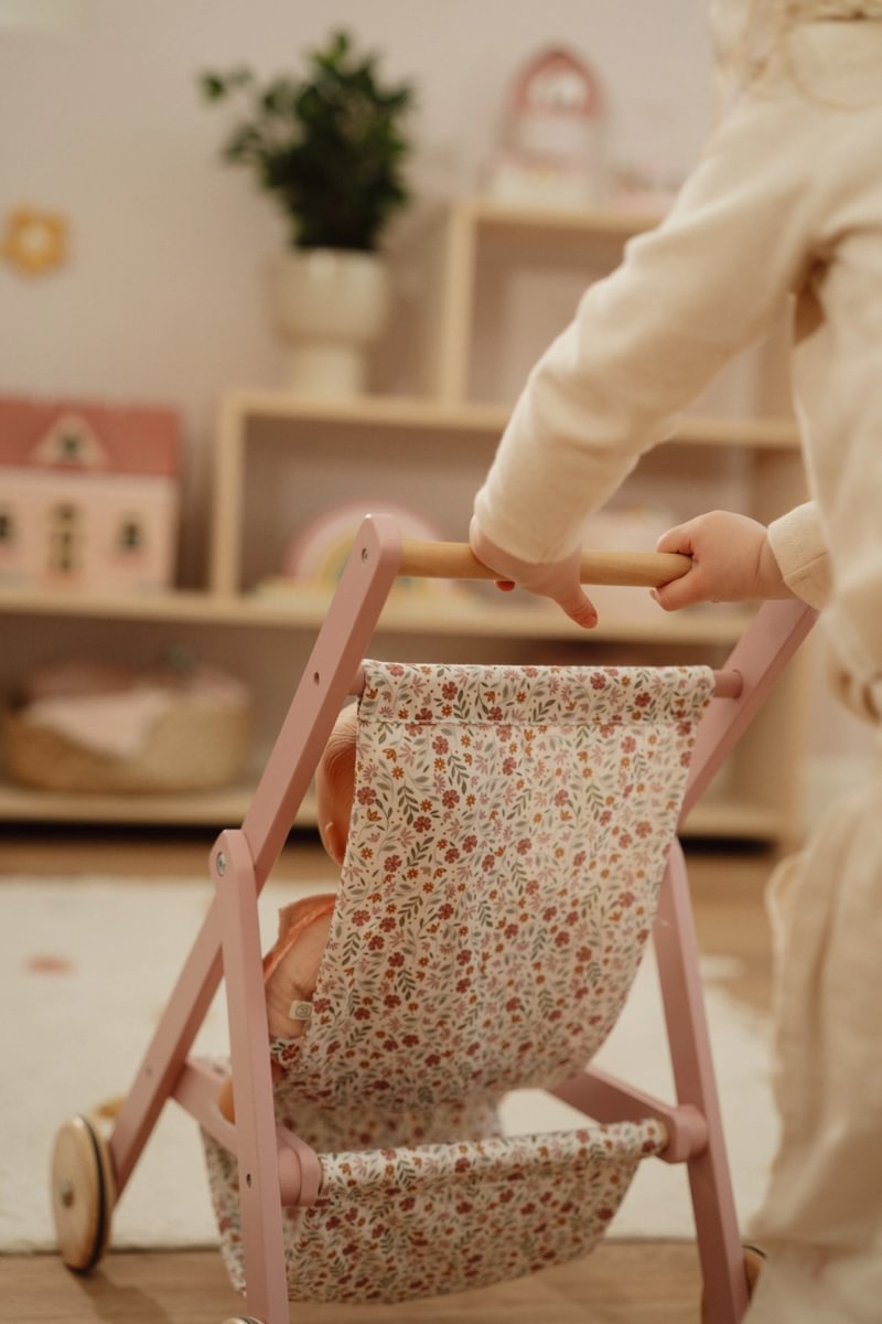 Carrinho de brinquedo de madeira rosa com assento floral sendo empurrado por criança