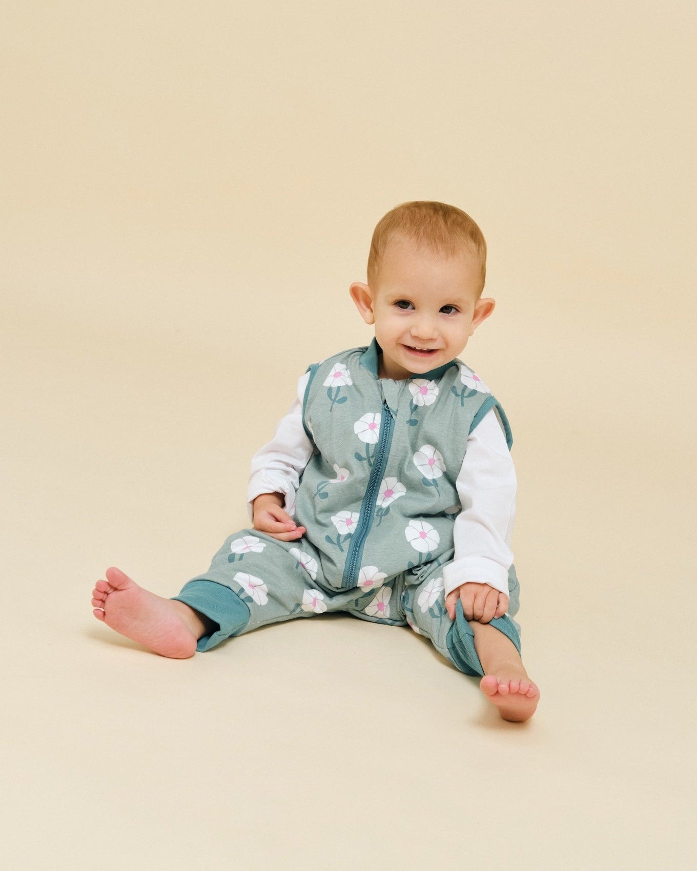 Bebé com babygrow verde acinzentado de flores sentado em fundo bege
