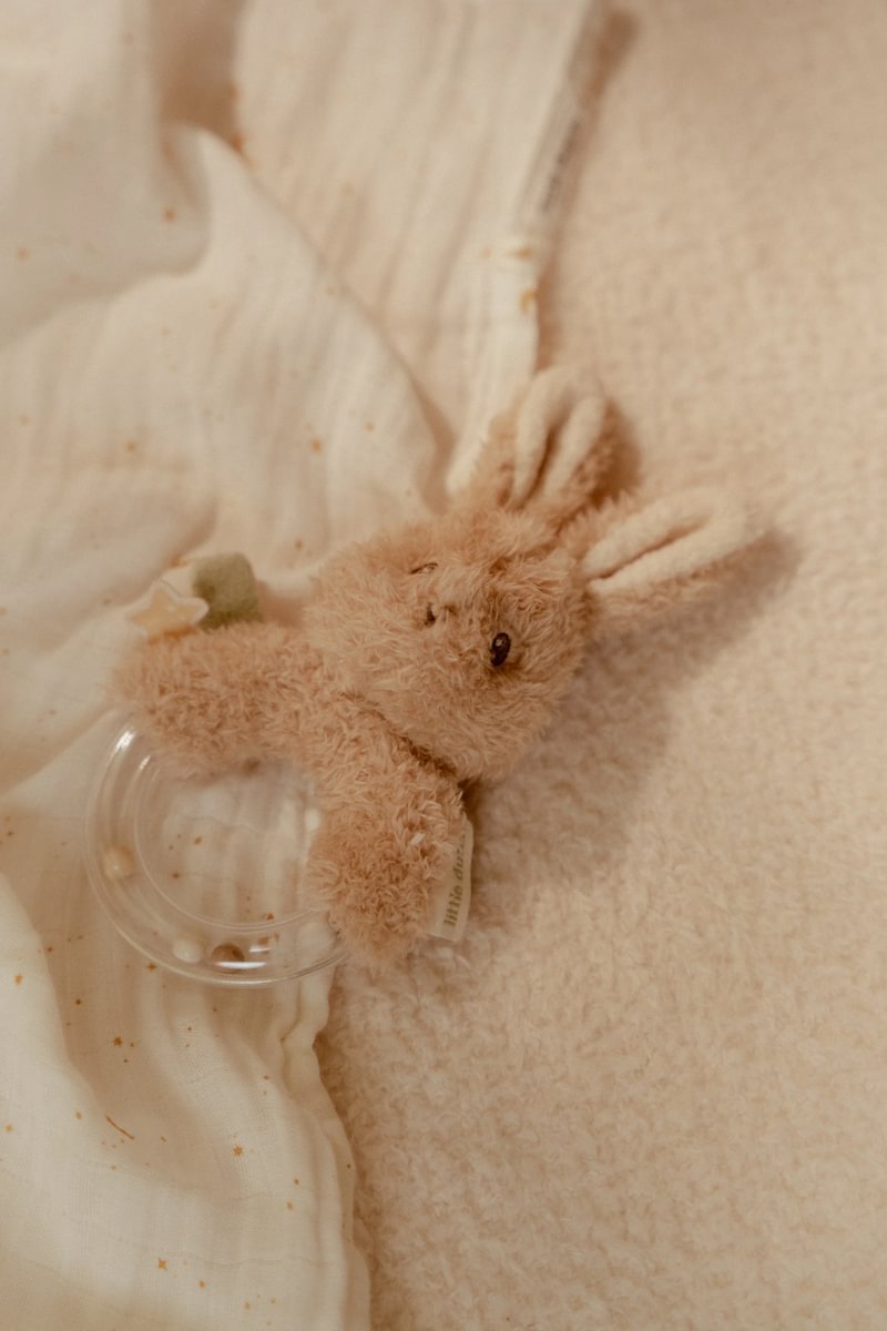 Mordedor de peluche castanho em forma de coelho com anel transparente sobre tecido branco com estrelas douradas