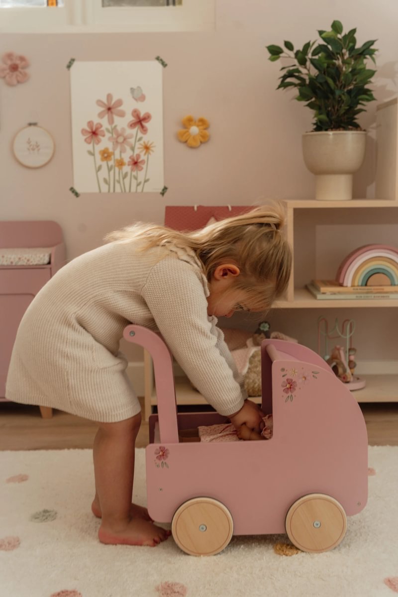 Criança a brincar com carrinho de brinquedo rosa com motivos florais num quarto infantil decorado