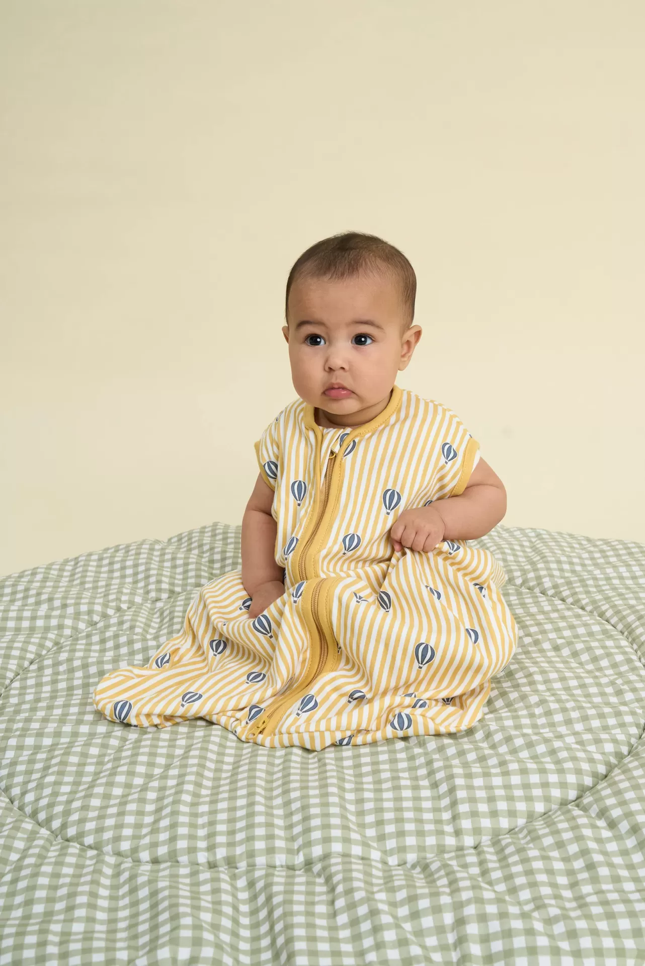 Bebé sentado com saco de dormir amarelo às riscas e balões azuis